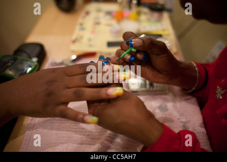 Keisha, un Antiguan nail designer vernici colorate di strati su unghie finte. Foto Stock