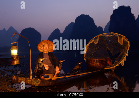 Pescatore con i cormorani su zattera di bambù di purple dawn e picchi di calcare sulla riva del fiume Li Yangshuo Cina Foto Stock