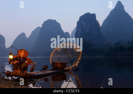 Cormorano pescatore lampada di illuminazione con gli uccelli sulla zattera di bambù all'alba e sharp ambiente carsico picchi sulla riva del fiume Li Yangshuo Cina Foto Stock