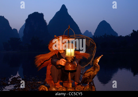 Cormorano pescatore lanterna di illuminazione con bird su zattera di bambù all'alba con silhouette di vette carsiche sulla riva del fiume Li Yangshuo Cina Foto Stock