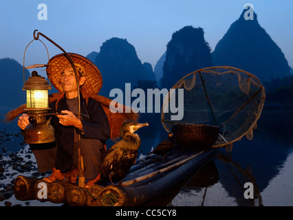 Pescatore con la lanterna su una zattera di bamboo con cormorani all'alba con ambiente carsico picchi sulla riva del fiume Li Yangshuo Cina Foto Stock