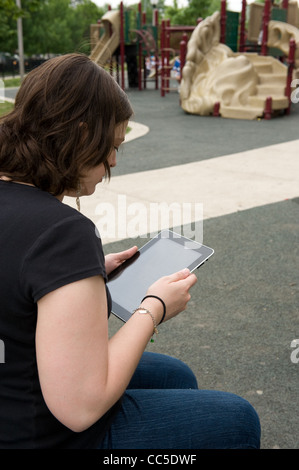 Caucasian donna seduta su una panchina nel parco leggendo il suo iPad Foto Stock