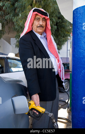 Arab / Arabian beduino di operatore della pompa (o il cliente) trattiene l'ugello della pompa mentre il riempimento di una vettura a benzina. Madaba, Giordania. Foto Stock