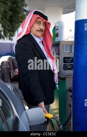 Arab / Arabian beduino di operatore della pompa (o il cliente) trattiene l'ugello della pompa mentre il riempimento di una vettura a benzina. Madaba, Giordania. Foto Stock