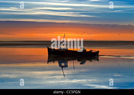 Una barca di gamberi torna a casa con la sua notte cattura come Una bella alba illuminata dal sole si rompe sull'estuario di Lytham Foto Stock