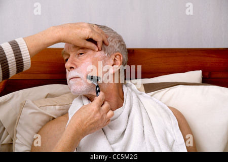 Un uomo nel suo 60's rasata da sua moglie/accompagnatore, a casa a letto Foto Stock
