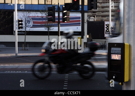 Vista su una strada che mostra un 'IN ATTESA' segno su un attraversamento pedonale e un motore ciclista passante Foto Stock