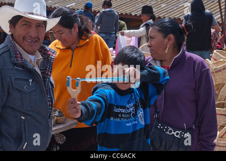 Un dodicenne ispanico boy tenta di eseguire una nuova slingshot in aria aperta nel mercato Saquisili, Ecuador. Foto Stock