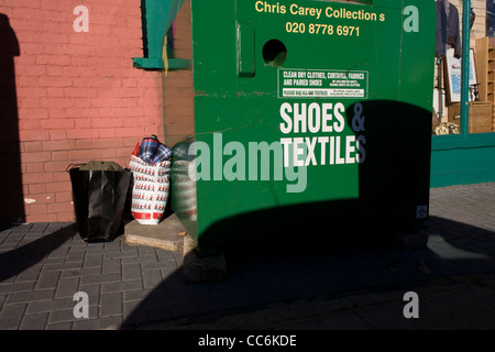 Sacchetti di abbigliamento di seconda mano sinistra in prossimità di una carità shop recipiente in una strada di Londra. Foto Stock