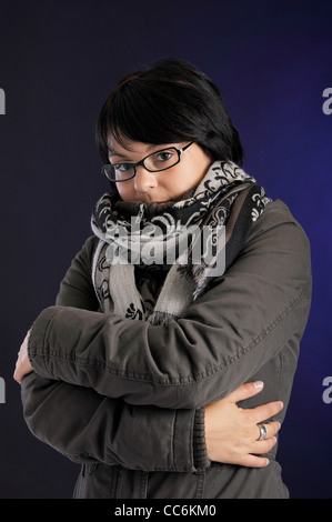 Giovane donna in winterclothes avente freddo. Su sfondo blu scuro Foto Stock