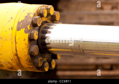 Un cilindro idraulico dipinto di giallo con un asta di cromo Foto Stock