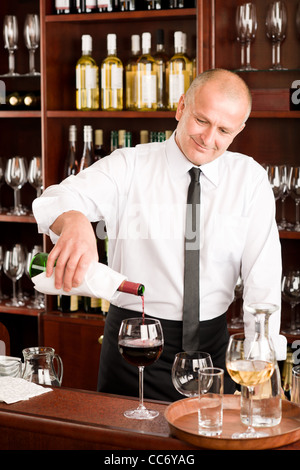 Presso il bar - cameriere versare il vino rosso in vetro ristorante Foto Stock