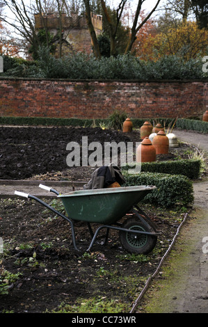 Ampio giardino essendo preparato per la semina la semina con carriola lavoratori giacca e vasi e fioriere in shot Foto Stock