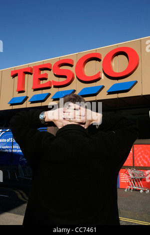 Un uomo tiene le mani dietro la testa davanti a un supermercato Tesco Foto Stock