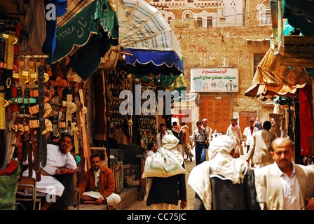 Yemen, Sanaa, persone che camminano nella trafficata strada del mercato da shop con edificio in background Foto Stock