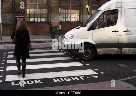 Una femmina di passeggiate attraverso una zebra crossing a Londra mentre un furgone attende Foto Stock