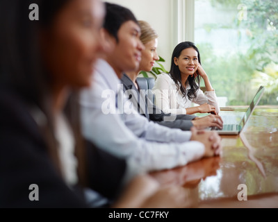 Bella giovane donna asiatica lavorando e sorridente alla telecamera durante la riunione di affari con i colleghi. Foto Stock
