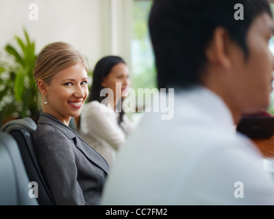 Giovane e bella donna bionda lavora come manager e sorridente alla telecamera durante la riunione di affari con i colleghi. Foto Stock