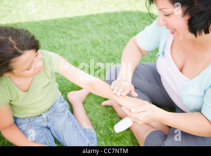 Madre ispanica mettendo sunscreen sulla figlia Foto Stock