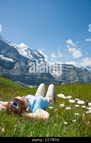 Donna sdraiata su erba sul lato montagna, Oberland bernese, Svizzera Foto Stock