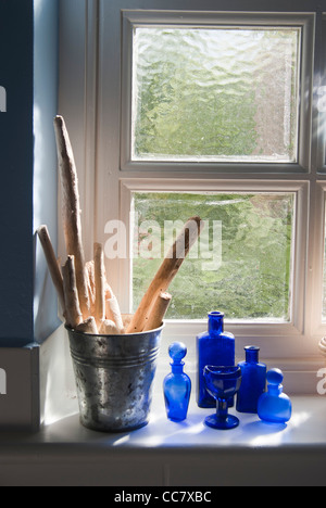 Pezzi di driftwood in una pentola di metallo e il blu cobalto bottiglie visualizzata su un davanzale Foto Stock