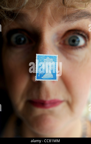 Donna di mezza età vicino la faccia con un britannico secondo 2a classe francobollo incollato al modello di naso Foto Stock