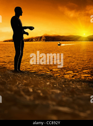 Uomo in piedi sulla sabbia bagnata a bright sfondo al tramonto Foto Stock
