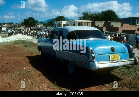 Un vecchio American automobile parcheggiata accanto a una strada sterrata in Trinidad, Cuba. La gente in background sono di ritorno da un giorno di maggio Rally Foto Stock