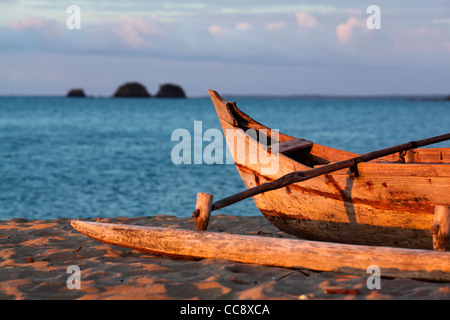 Una spiaggiata outrigger piroga, o pirogue, malgascia imbarcazione a vela, con tre piccole isole in background al tramonto Foto Stock