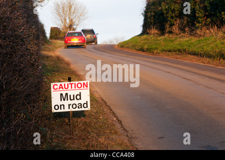 'Attenzione fango sulla strada' segno su un paese di Norfolk lane con due vetture in distanza. Foto Stock