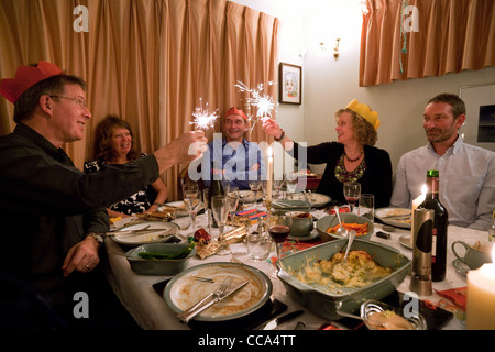 Cinque adulti al tavolo da pranzo con fuochi d'artificio al coperto in una cena per le celebrazioni di Capodanno a casa, Regno Unito Foto Stock