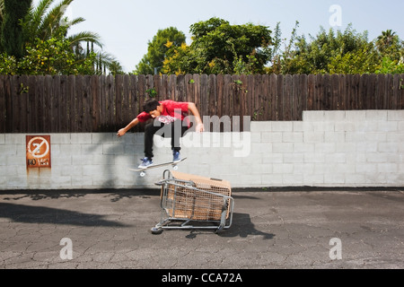 Uomo su skateboard saltando su un carrello della spesa Foto Stock