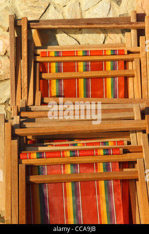 Strisce di legno sedie a sdraio appoggiata contro un muro di pietra di sole Foto Stock