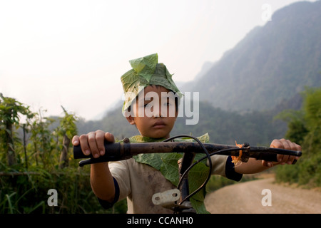 Un giovane ragazzo in sella ad una bicicletta è che indossa un costume fatto di foglie in prossimità delle Grotte di Vang Vieng, Laos. Foto Stock