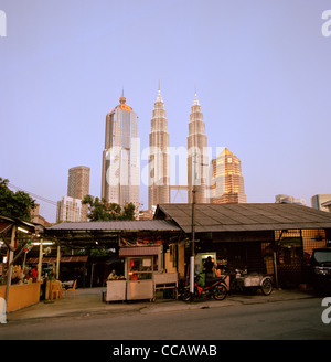 Il tramonto e la notte scende come le Torri Petronas incombono su di Kampung Baru nella città di Kuala Lumpur in Malesia in Estremo Oriente Asia sud-orientale. Città Travel Foto Stock