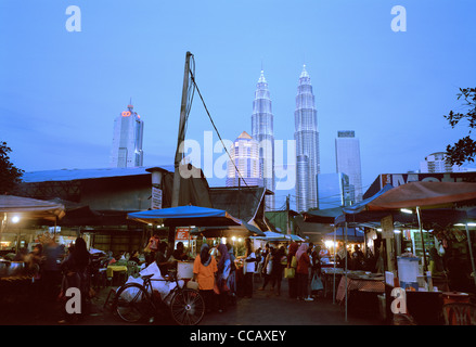 Il tramonto e la notte scende come le Torri Petronas incombono su di Kampung Baru nella città di Kuala Lumpur in Malesia in Estremo Oriente Asia sud-orientale. Città Travel Foto Stock