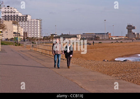 Vista frontale di una coppia di anziani camminare tenendo le mani lungo il lungomare di Folkestone nel Kent REGNO UNITO vestito di cappotti Foto Stock