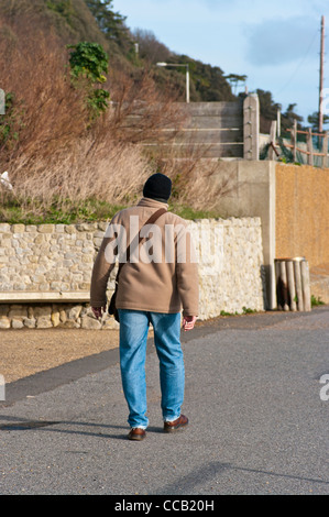 Vista posteriore di un uomo a piedi indossando un cappotto invernale giacca blu jeans e un cappellino Foto Stock