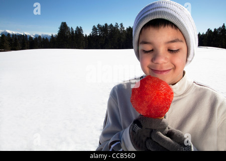 Ragazzo 10 -12 anni di mangiare un cono di neve su una giornata invernale all'esterno. Foto Stock