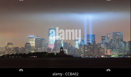 New York City Manhattan skyline del centro panorama di notte con la statua della libertà e i fasci di luce Foto Stock