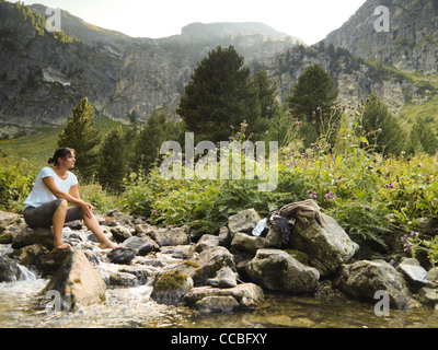 Una giovane e bella escursionista in appoggio su di una roccia in un alto fiume di montagna Foto Stock