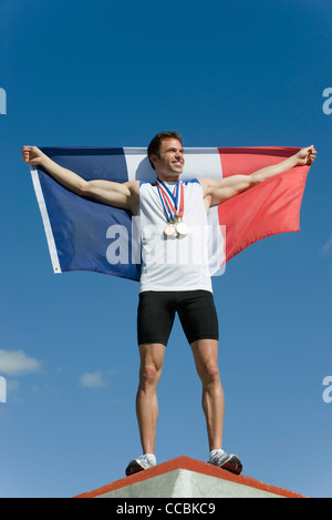 Atleta maschio essendo onorato sul podio, mantenendo la bandiera francese Foto Stock