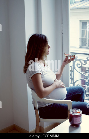Donna incinta di mangiare pane tostato con marmellata Foto Stock