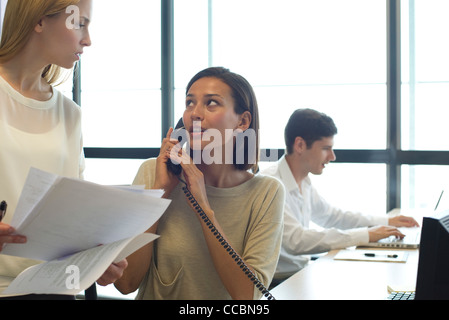 Imprenditrice parlando al telefono in ufficio, guardando a un collega Foto Stock