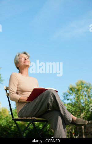 Senior donna seduta all'aperto con Libro, godendo il calore del sole Foto Stock