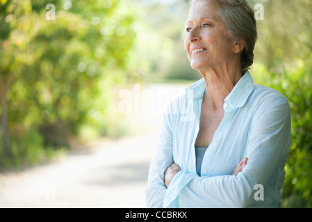 Senior donna sorridente e cercando in distanza Foto Stock