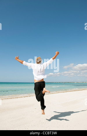 L'uomo jumping midair sulla spiaggia, vista posteriore Foto Stock