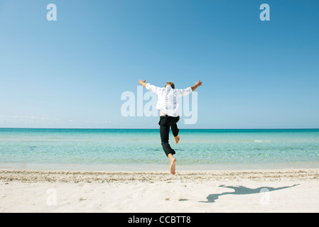 L'uomo jumping midair sulla spiaggia, vista posteriore Foto Stock