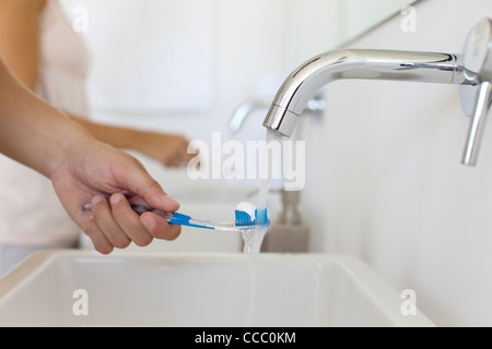 Uomo con spazzolino da denti sotto il rubinetto, ritagliato Foto Stock