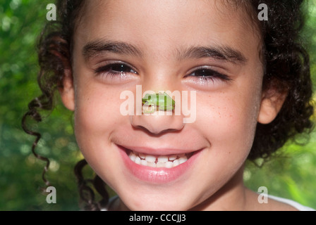 Ragazza giovane con un Australian ranocchio verde (Litoria caerulea) seduta sul suo naso Foto Stock